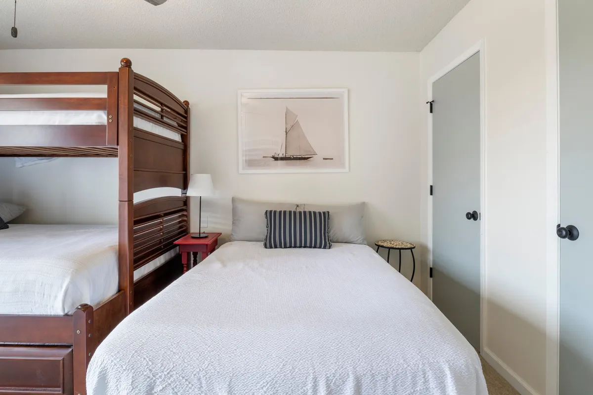 A cozy guest bedroom designed for families or groups, featuring a bunk bed, a single bed, framed artwork, and a bedside table. The arrangement is functional yet inviting, making it easy for multiple guests to feel at home.