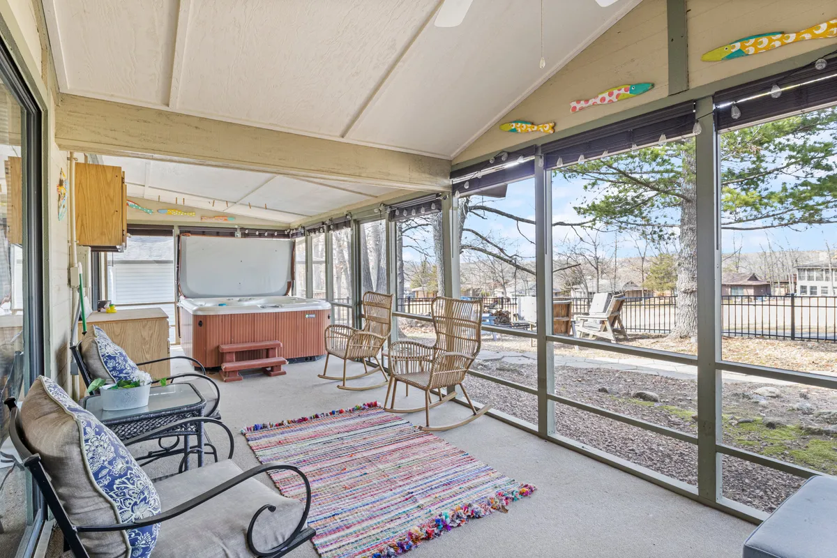 The image showcases the inviting exterior of a lake home, featuring a bubbling hot tub and a pair of cozy rocking chairs set on a stylish area rug. Decorative fish accents add a playful touch, while the view opens up to lush golf course greens and glimmers of the lake beyond. The setting exudes relaxation, perfect for stargazing, sipping morning coffee, or gathering with friends around a fire pit.