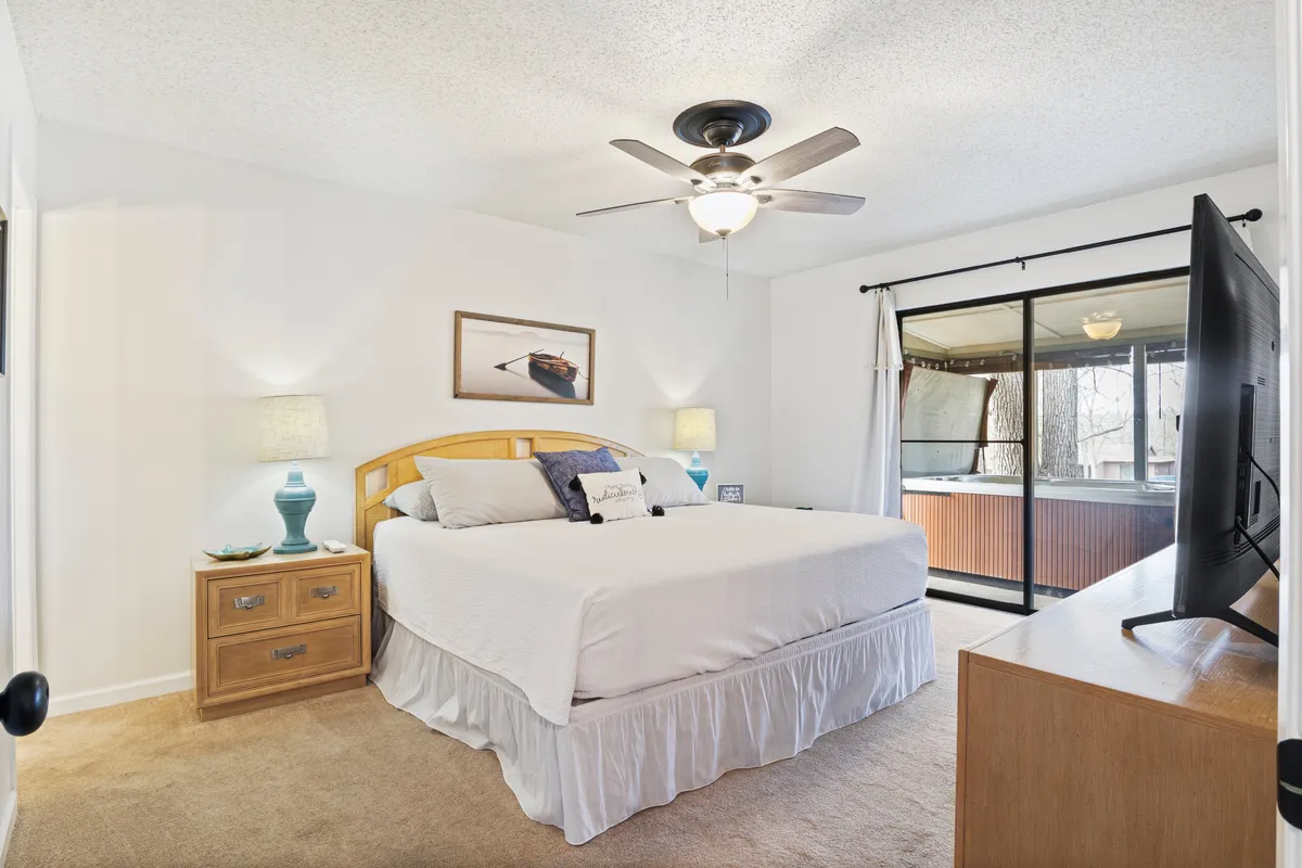 A tranquil bedroom with a large bed, a television, a sliding glass door that lets in abundant natural light, a nightstand, and decorative wall art. The room feels both modern and comfortable, offering views outside and space for unwinding.