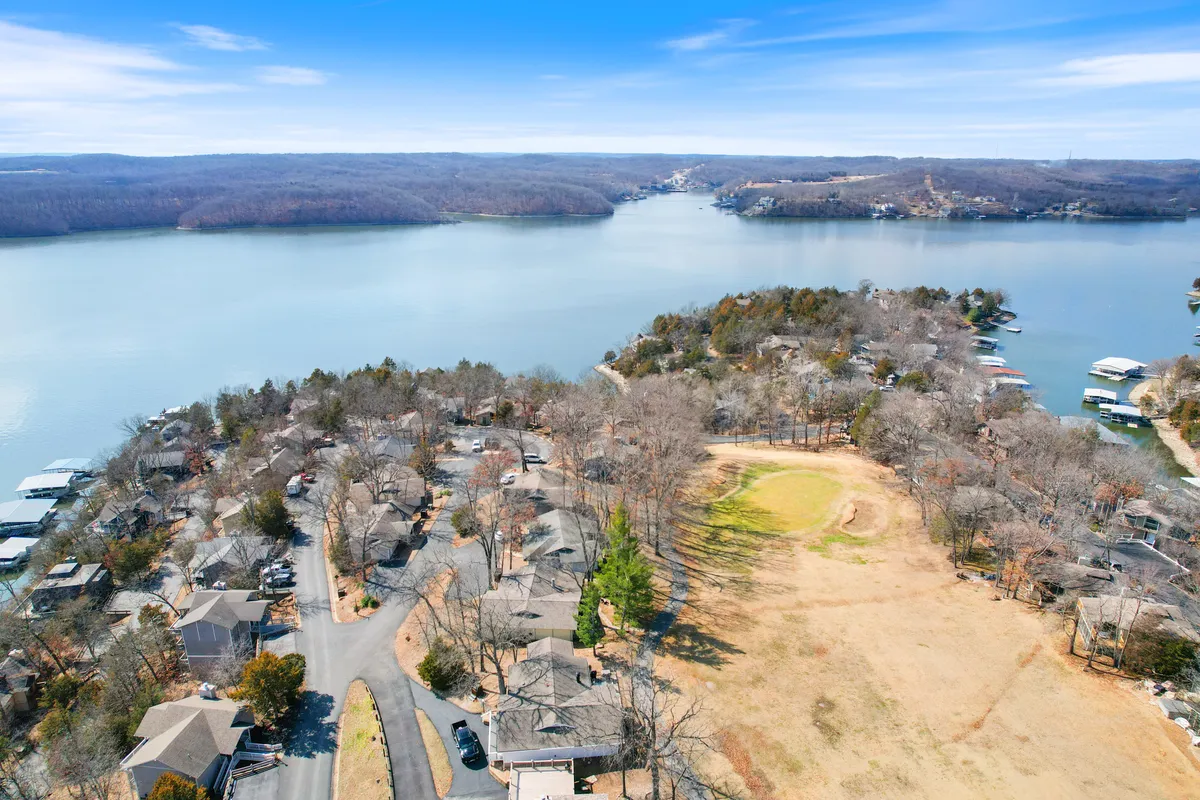 A sweeping view of the lake bordered by homes and open green spaces, with roadways weaving through the landscape. The tranquil water and wide skies suggest opportunities for boating, fishing, and gathering at the shoreline.