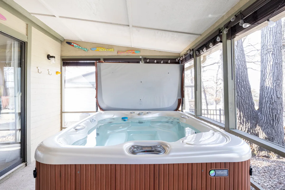 A cozy, inviting screened-in porch with a prominent hot tub surrounded by large windows that blur the lines between indoors and out. Decorative fish accents and glimpses of nature just beyond the screen enhance the sense of relaxation and year-round enjoyment.