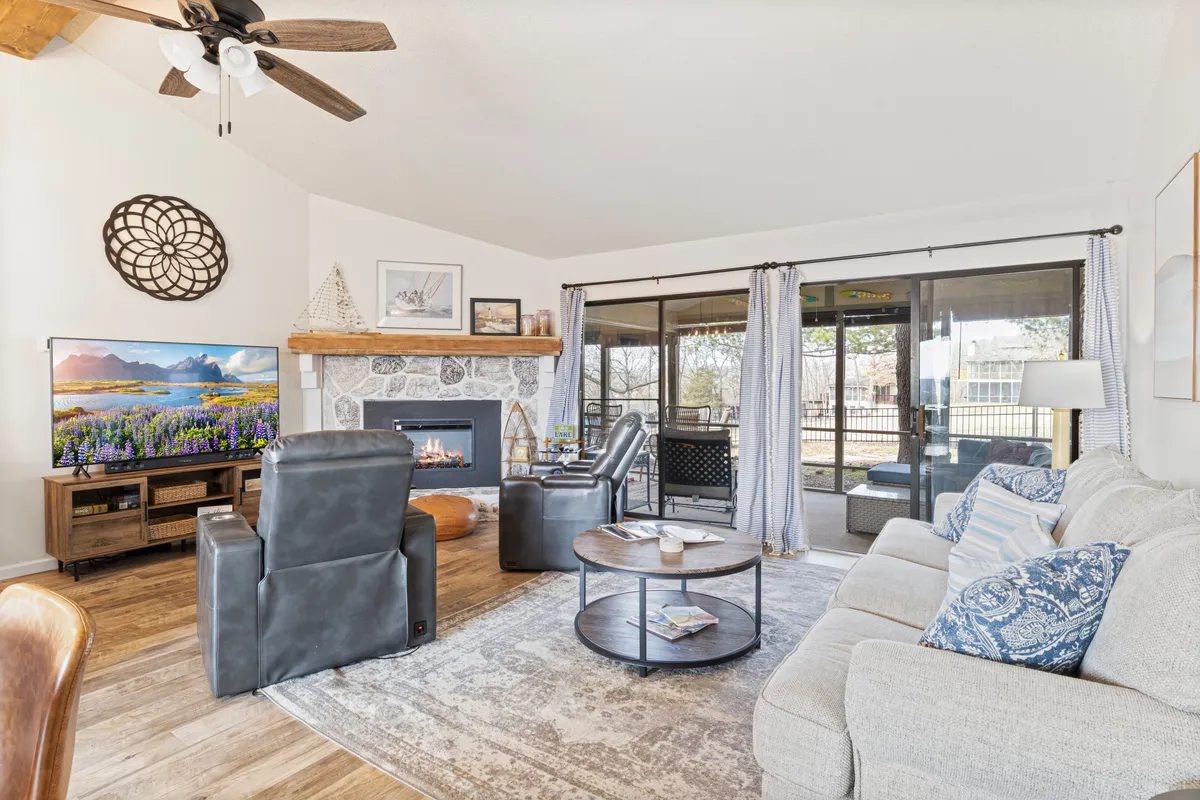 A spacious living room featuring a comfortable sofa, a coffee table, and a modern electric fireplace. Large sliding glass doors let in natural light and offer a glimpse of the outdoors, while the arrangement of furnishings encourages conversation and relaxation.
