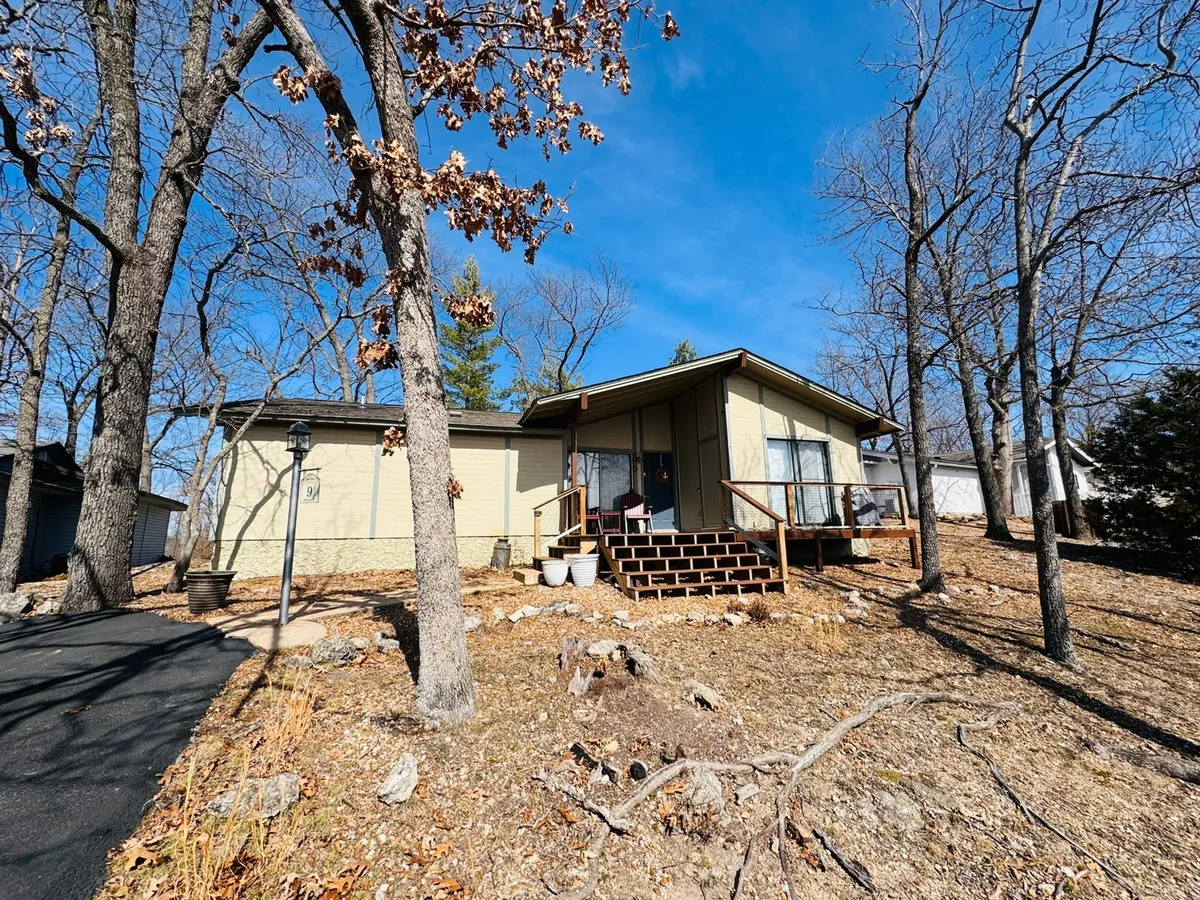 A welcoming front porch surrounded by large windows and leafy trees, perched above a rocky landscape. The scene radiates serenity and offers glimpses of the tranquil natural setting, perfect for a peaceful getaway. The porch suggests opportunities for relaxing mornings with coffee, stargazing at night, or intimate evenings for couples.
