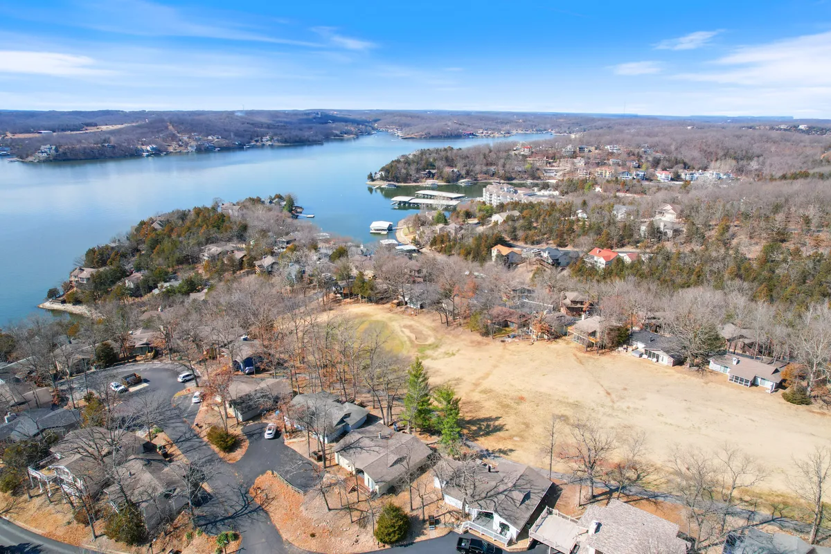 A tranquil view over the lake, dotted with houses, open fields, and surrounded by rolling hills. The scene captures the calm waters at sunset, hinting at opportunities for boating, fishing, picnicking, and soaking in nature's beauty. The expansive feel invites thoughts of a day spent outdoors enjoying the lake and its amenities.