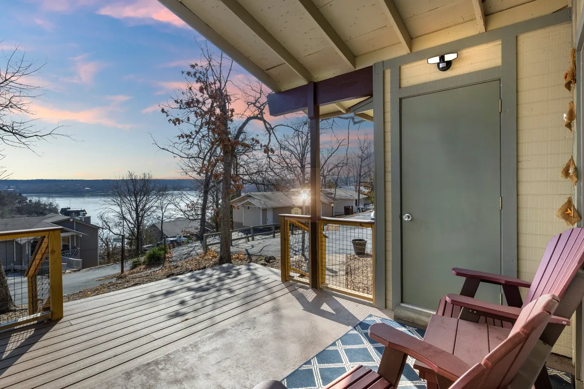 A peaceful exterior view of the front porch featuring wooden chairs facing out toward the lake, with a decorative door and hints of the tranquil water in the background. Morning light bathes the area, evoking a sense of calm and connection to the lake.