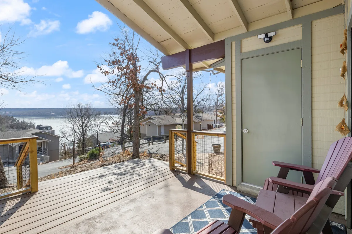 A wooden deck furnished with Adirondack chairs overlooking a peaceful body of water. The view includes natural surroundings and hints at opportunities for socializing outdoors, taking in sunsets, and enjoying the lake lifestyle.
