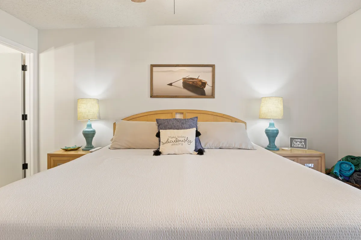 A serene bedroom featuring a well-made bed with decorative pillows, matching nightstands with lamps, and tasteful wall art. Soft natural light filters through unseen windows, creating a welcoming and peaceful atmosphere ideal for relaxation and rest.