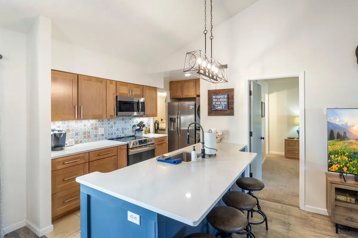 This image features a modern kitchen with a central island countertop, sleek appliances, colorful backsplash, and inviting wood cabinets. The space is clearly designed for cooking, entertaining, and family gatherings, emphasizing warmth and togetherness.